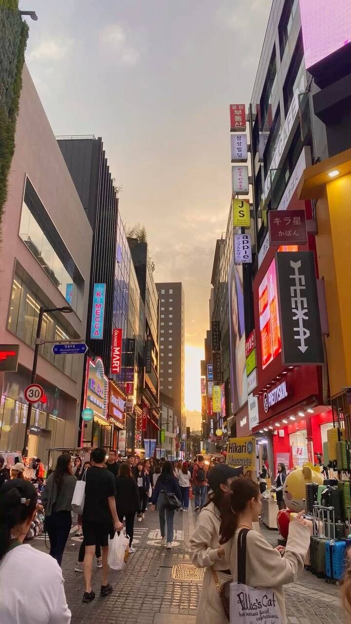 Calle comercial de Myeongdong al atardecer con multitud y letreros luminosos, Seúl